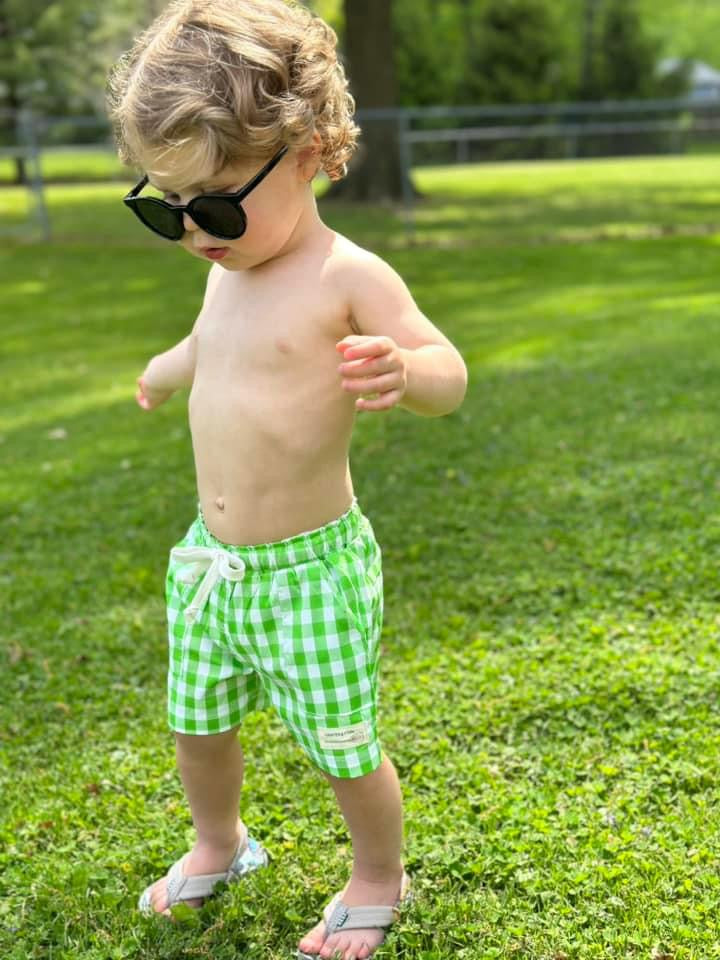 Little boy wearing wayfarer sunglasses and lime green gingham swim shorts